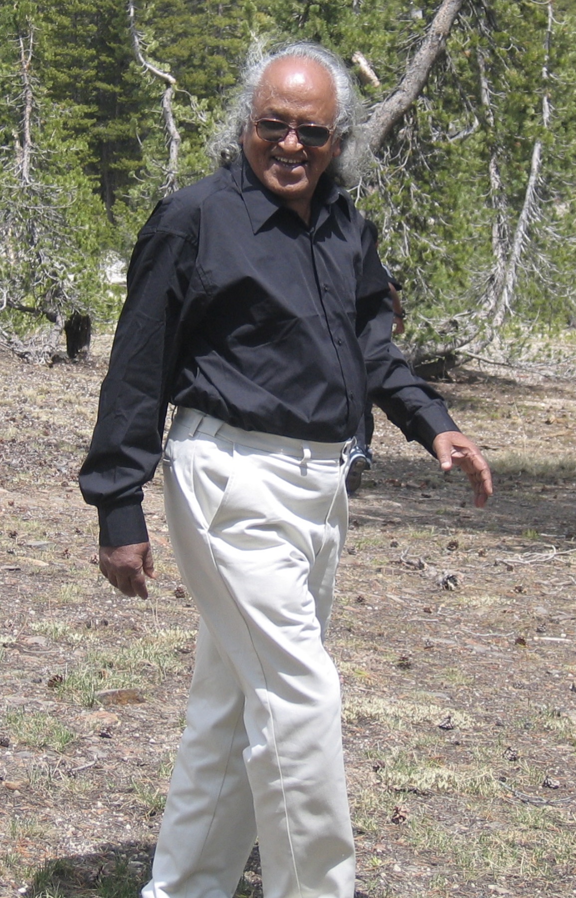 Dr. Gokulananda Das walking through a pine forest, smiling